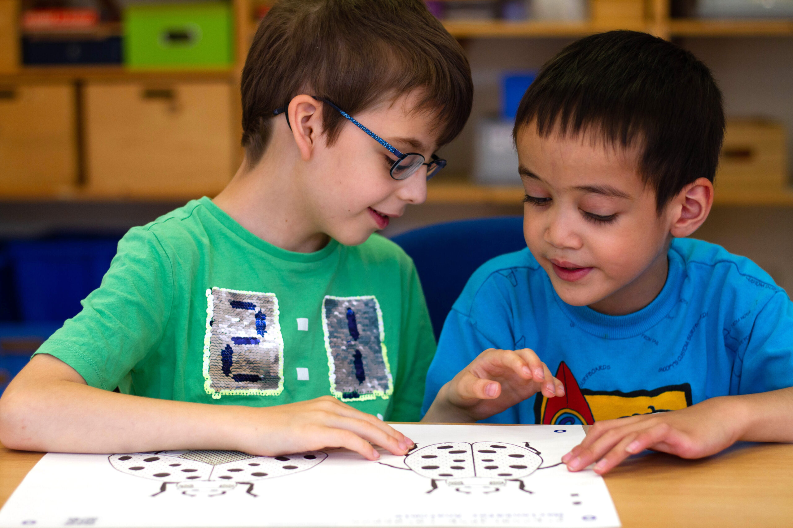 11Zwei kleine Jungen sitzen vor einer taktilen Grafik, die den Marienkäfer erklärt. Two little boys sit in front of a tactile graphic that explains the ladybug.