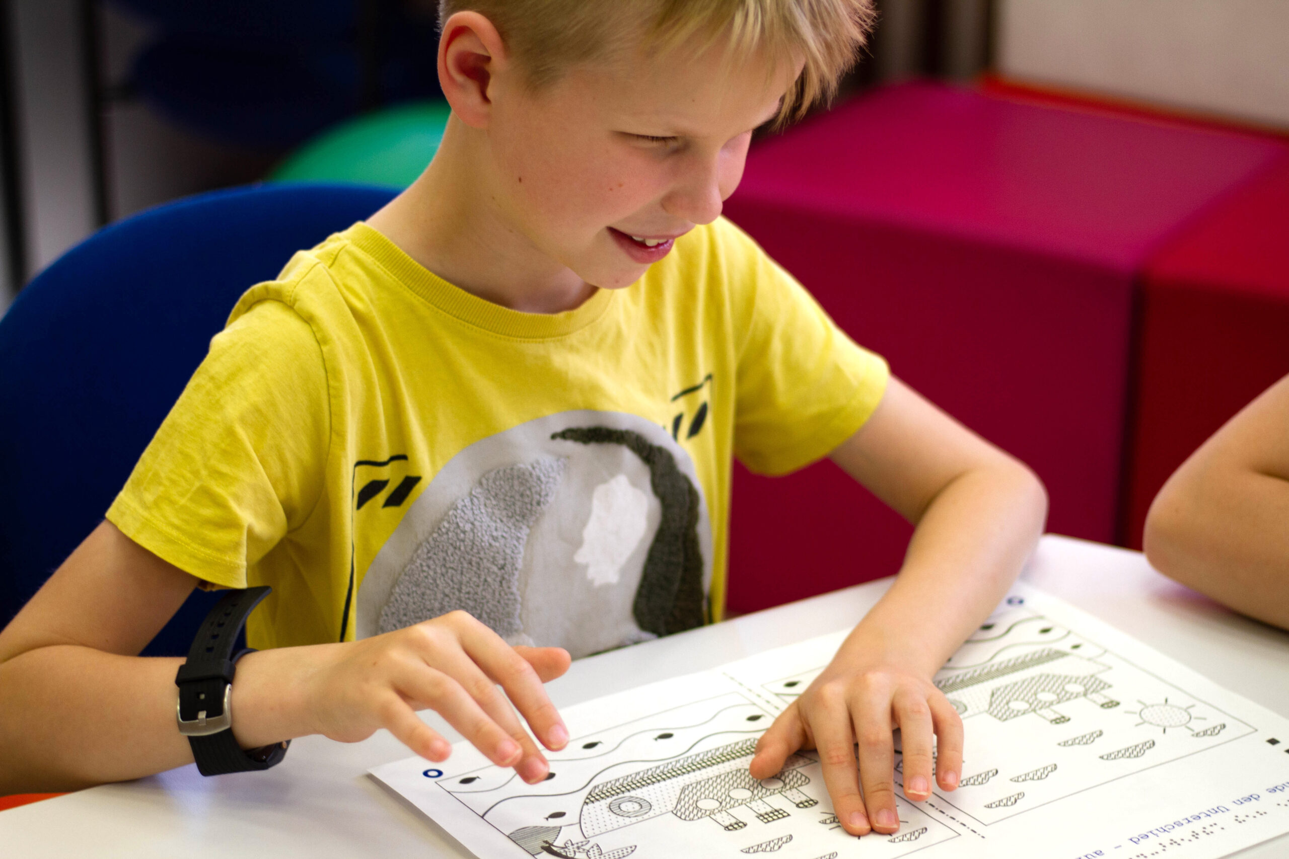 11Vor einem taktilen Vergleichsspiel sitzt ein vergnügter Junge. An amused boy sits in front of a tactile comparison game.